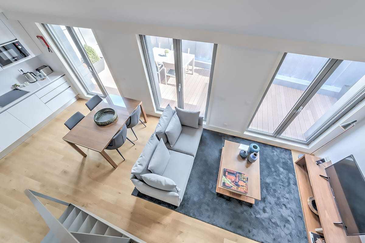 A modern apartment with a kitchen, dining area, and living space. It features large windows, a staircase, and a flat-screen TV.