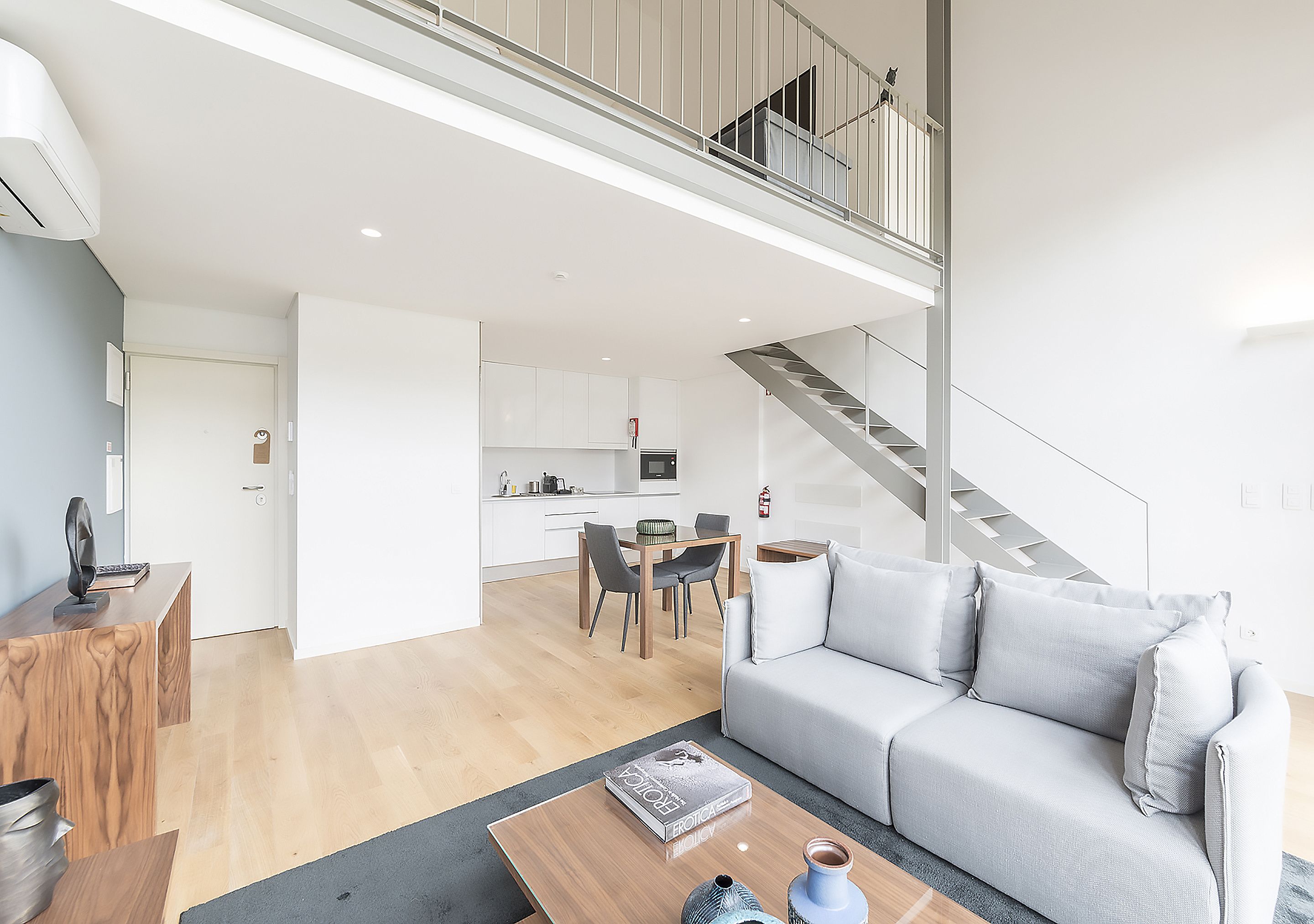 Un salon moderne avec un canapé gris, une table basse en bois et un escalier menant à un niveau supérieur.