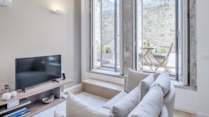 A modern living room with a flat-screen TV, a sofa, and a dining area visible through large windows.