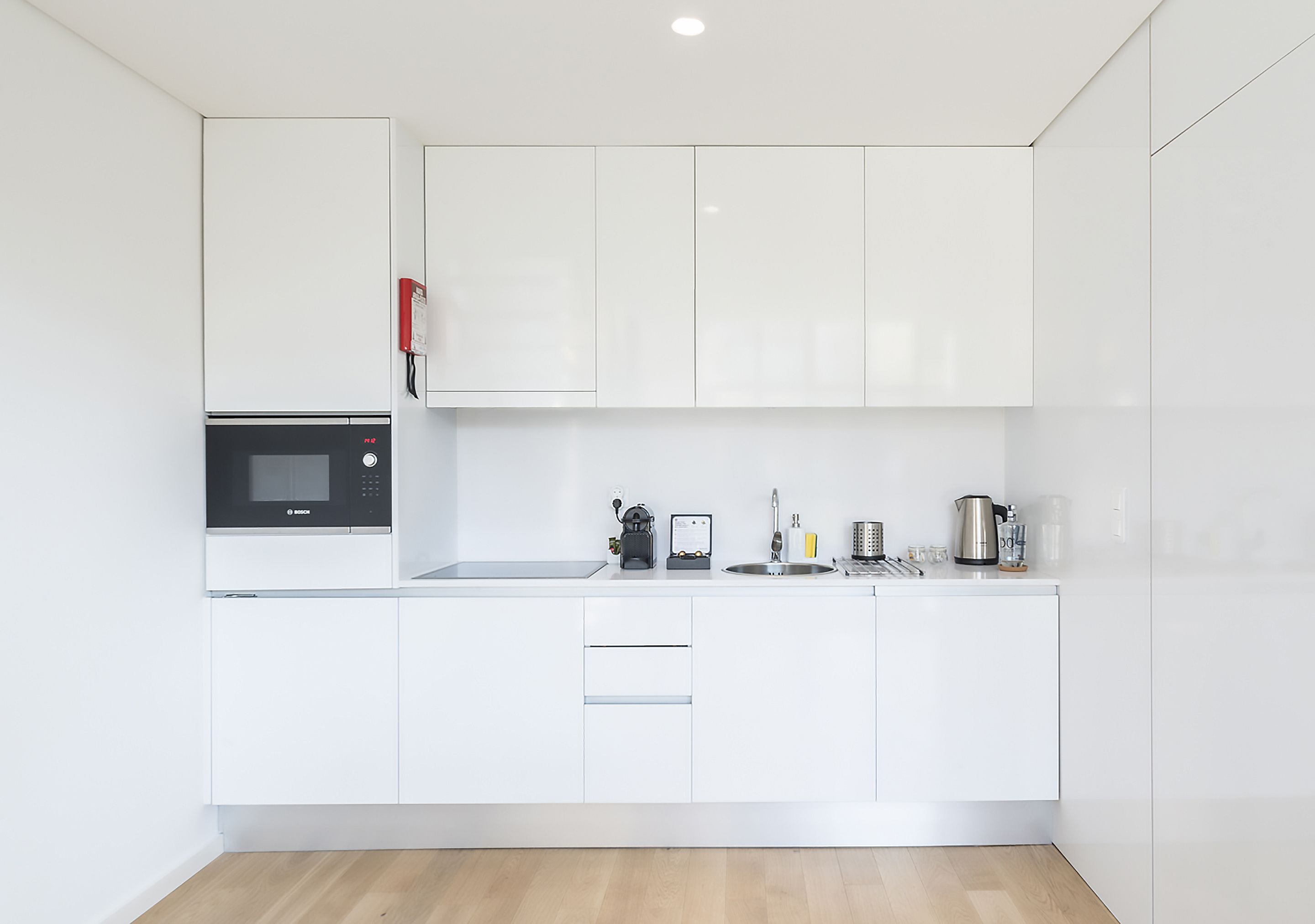 A modern kitchen with white cabinetry, a built-in microwave, a coffee machine, and a kettle.