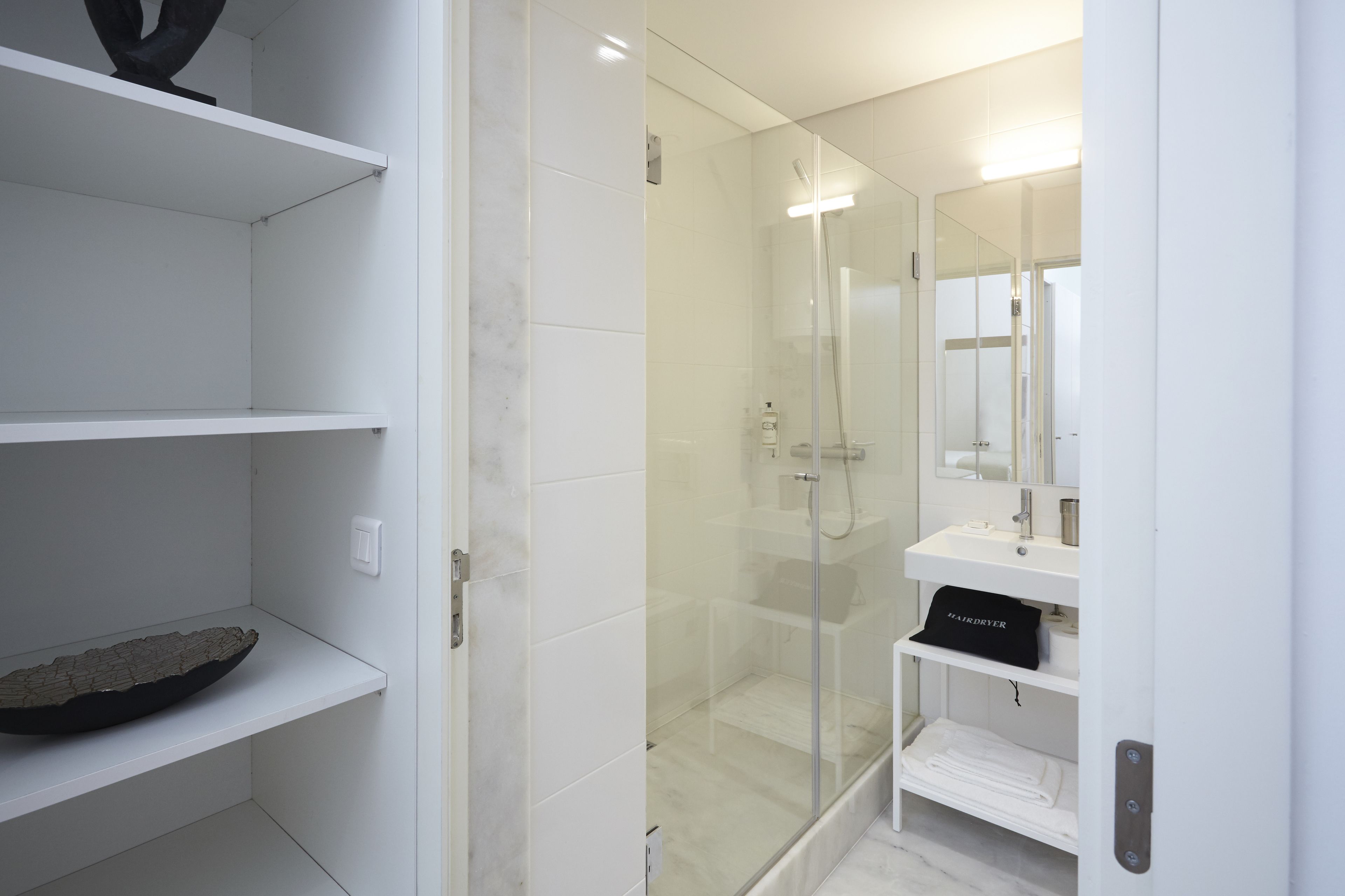 A modern bathroom with a glass-enclosed shower, white tiled walls, and a minimalist design.