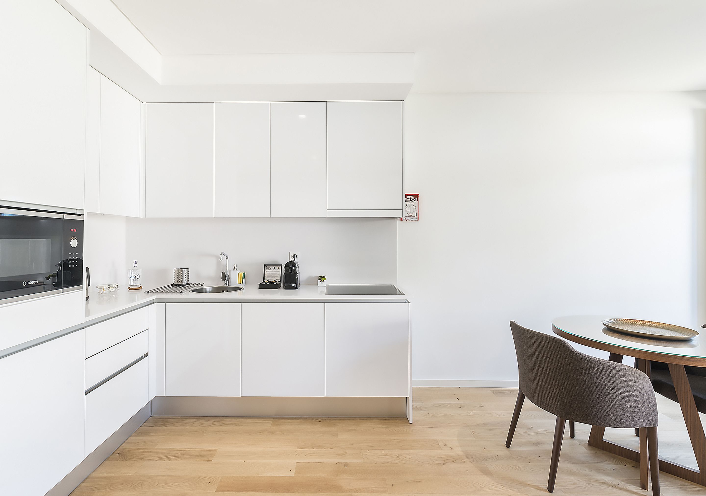 A modern kitchen with white cabinets, a Bosch microwave, and a dining area with a round table and chairs.