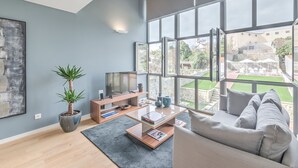 A modern living room with a large window, a flat-screen TV, a potted plant, and a grey sofa.