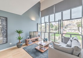 Una sala de estar moderna con un ventanal grande, un televisor de pantalla plana, una planta en maceta y un sofá gris.