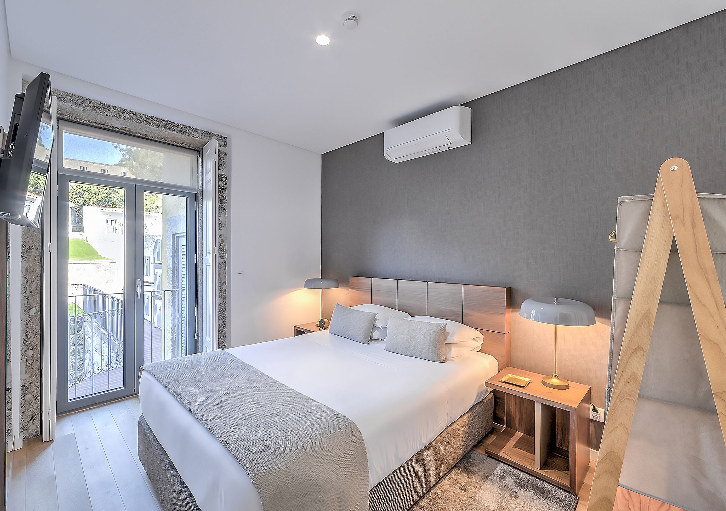 Une chambre moderne avec un grand lit, des lampes de chevet, un téléviseur et une vue sur l’extérieur.