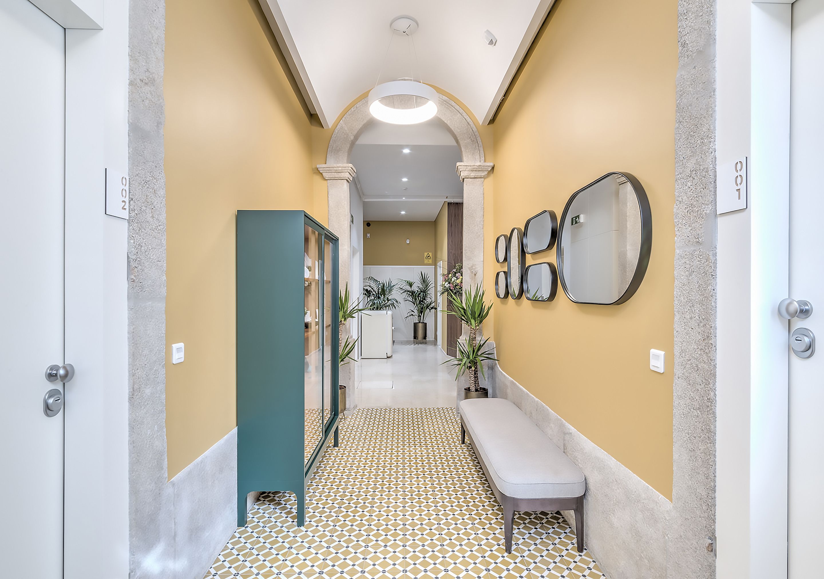 A hallway with a patterned floor, a bench, and multiple mirrors on the walls.