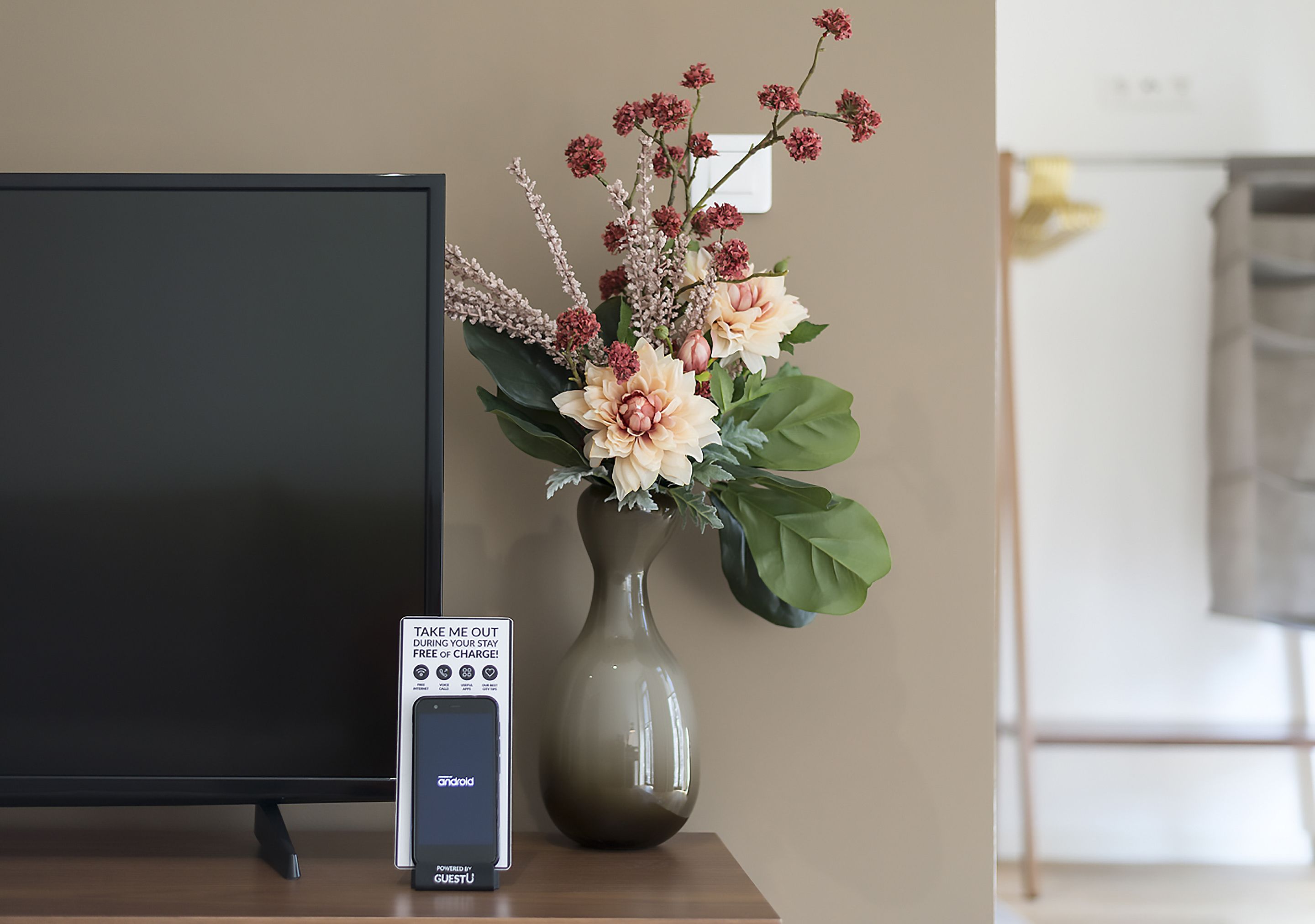 Et fladskærms-tv, en vase med blomster og et skilt om opladning af mobilenheder.