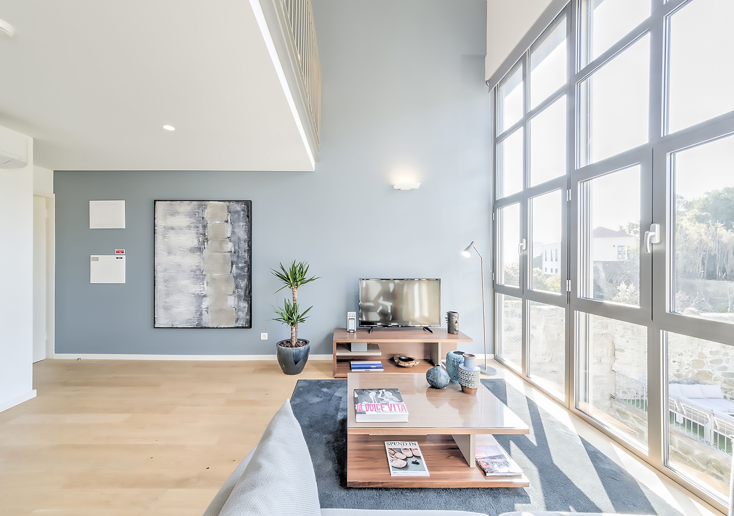 Een moderne woonkamer met een groot raam, een flatscreen-televisie, een salontafel en een bank.