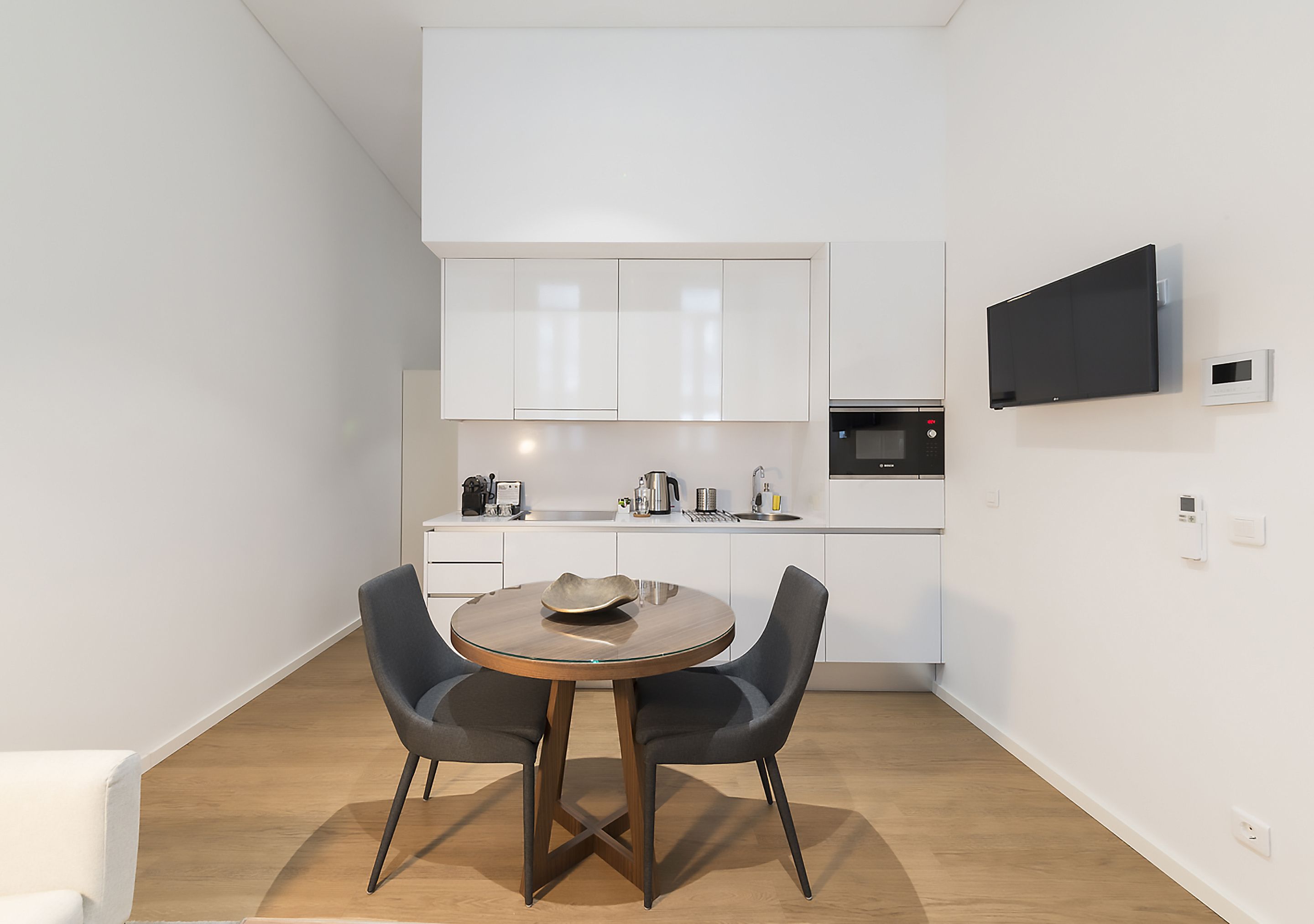 A modern kitchen with white cabinets, a microwave, and a flat-screen TV mounted on the wall.