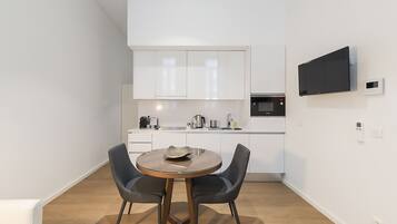 A modern kitchen with white cabinets, a microwave, and a flat-screen TV mounted on the wall.