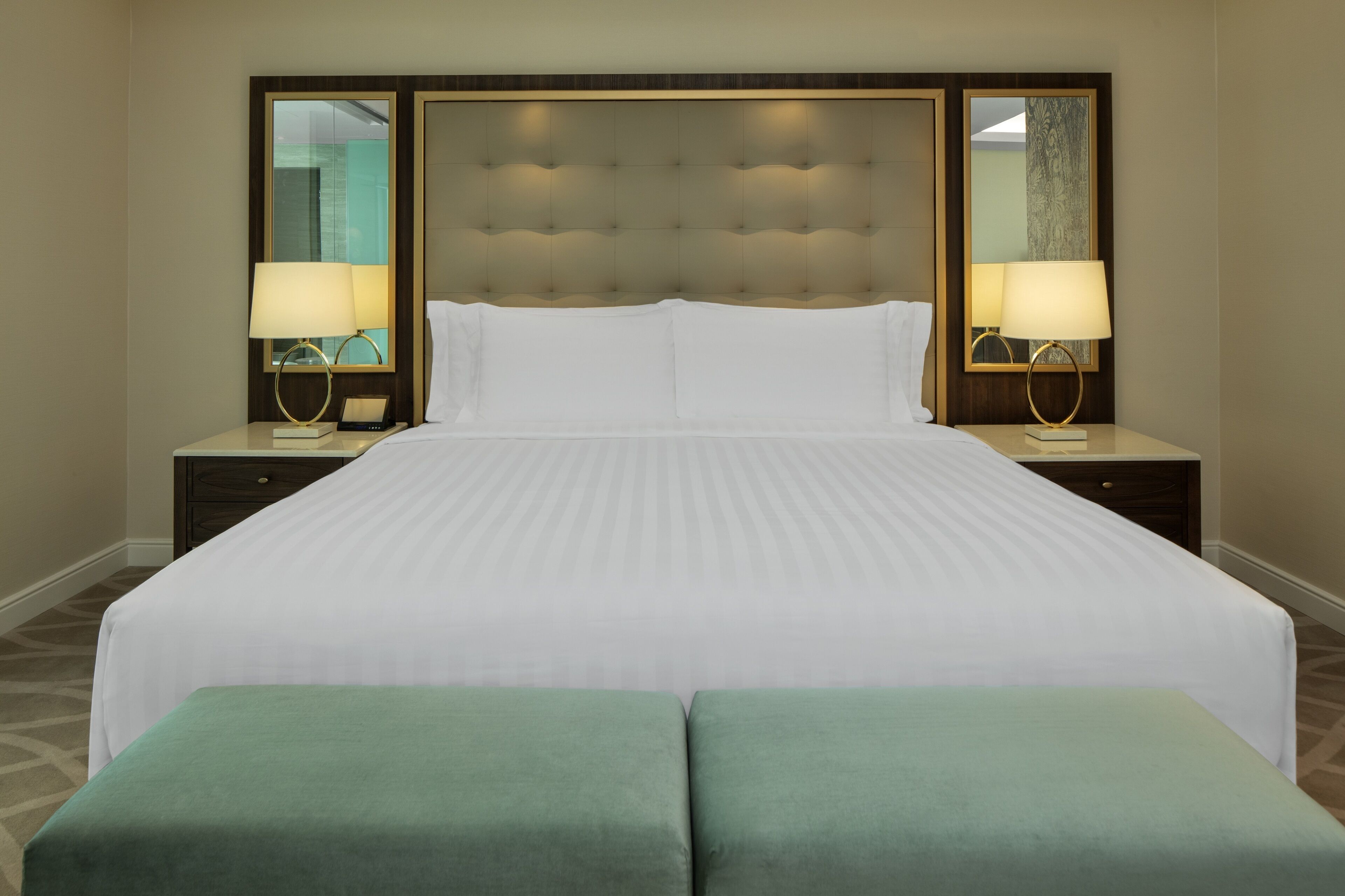 A hotel room with a large bed, two bedside tables with lamps, and a headboard with a mirror.