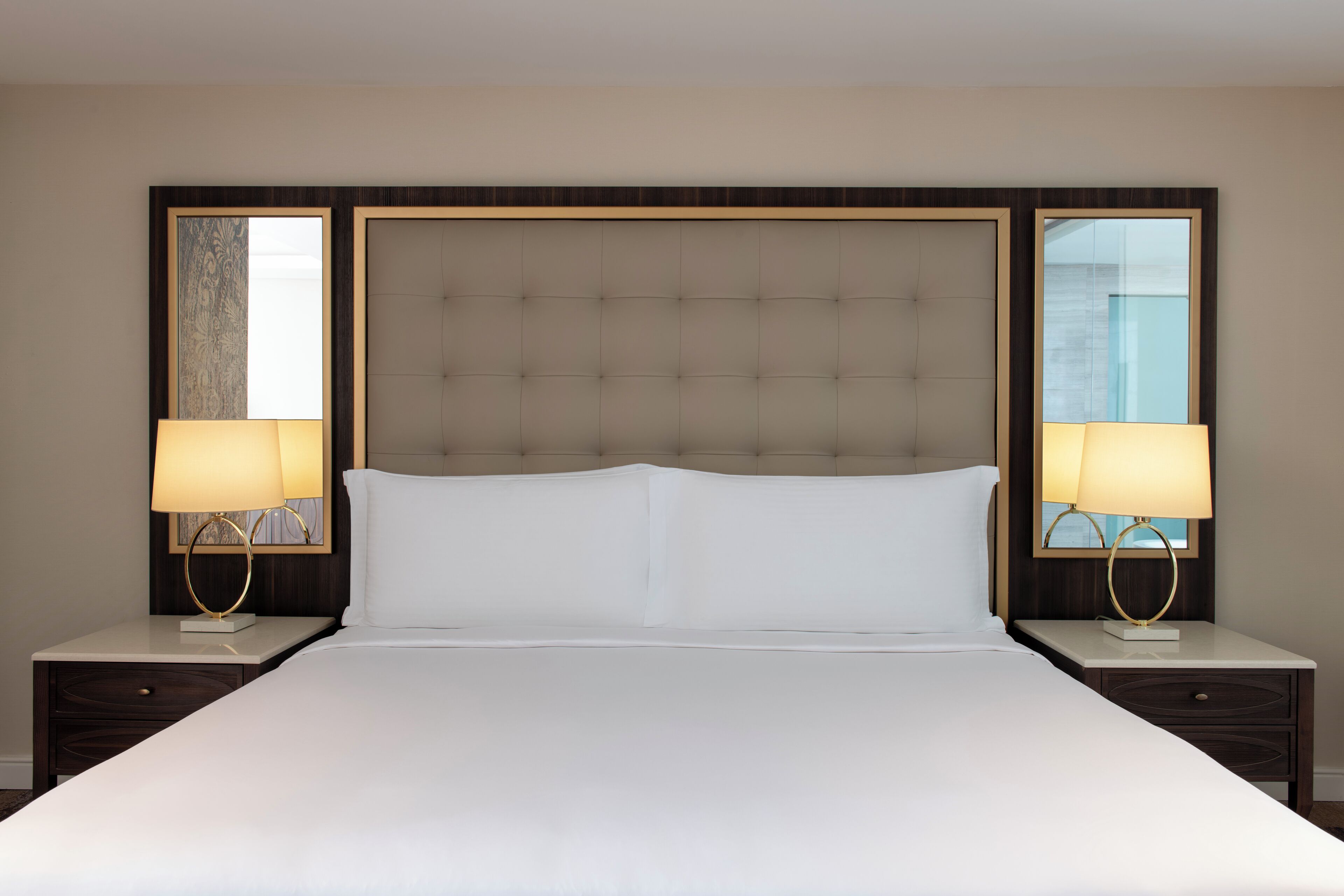 Ein Hotelzimmer mit einem großen Bett, zwei Nachttischen mit Lampen, einem Kopfteil und einem Spiegel an der Wand.