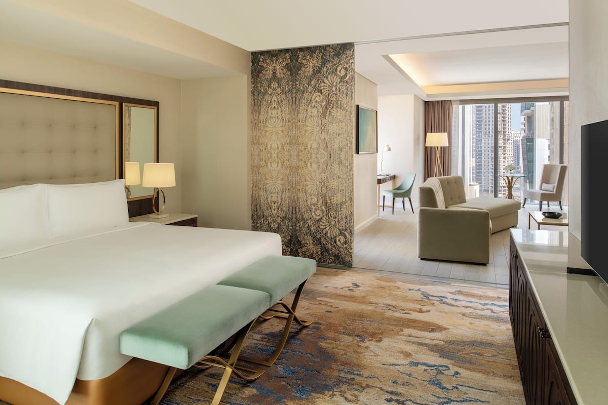 A hotel room with a large bed, a seating area with a sofa and chairs, a television, and a view of the cityscape.