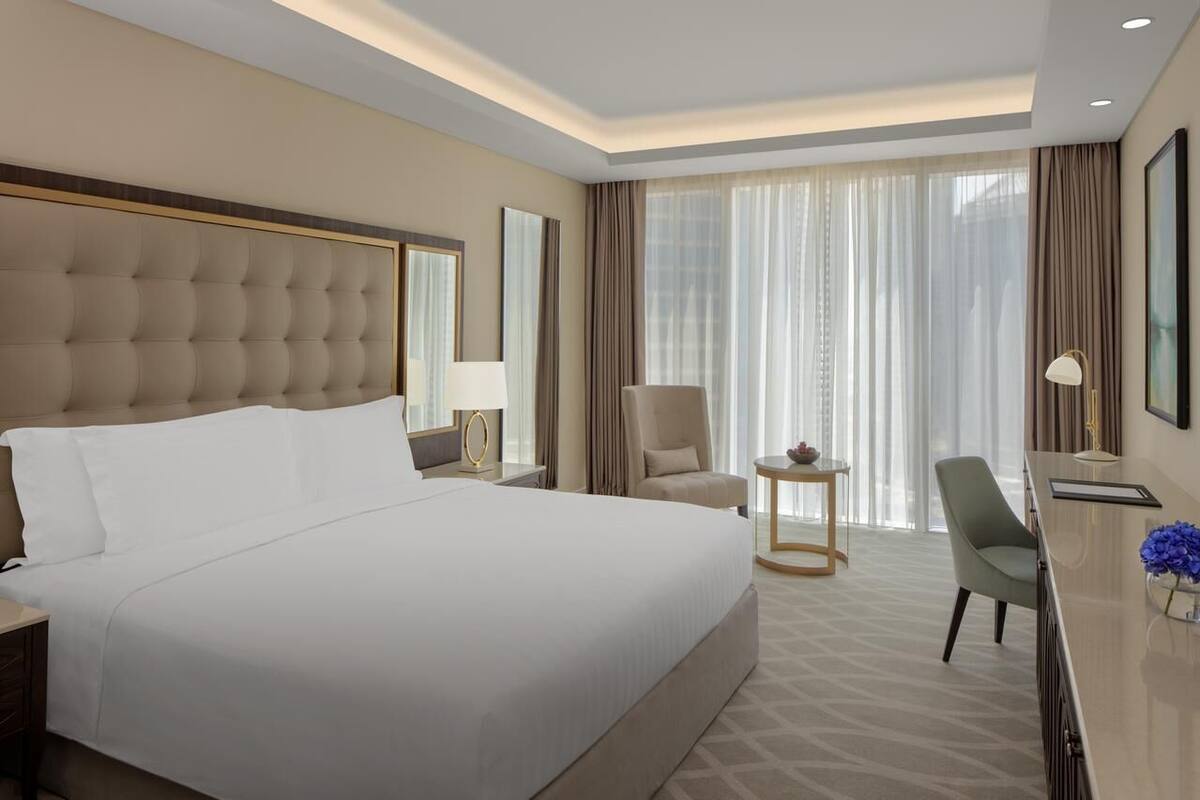 A hotel room with a large bed, a desk, a chair, and a small table.