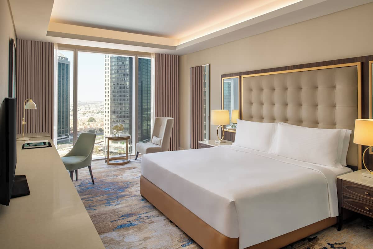 A hotel room with a large bed, a desk, a chair, and a view of tall buildings.