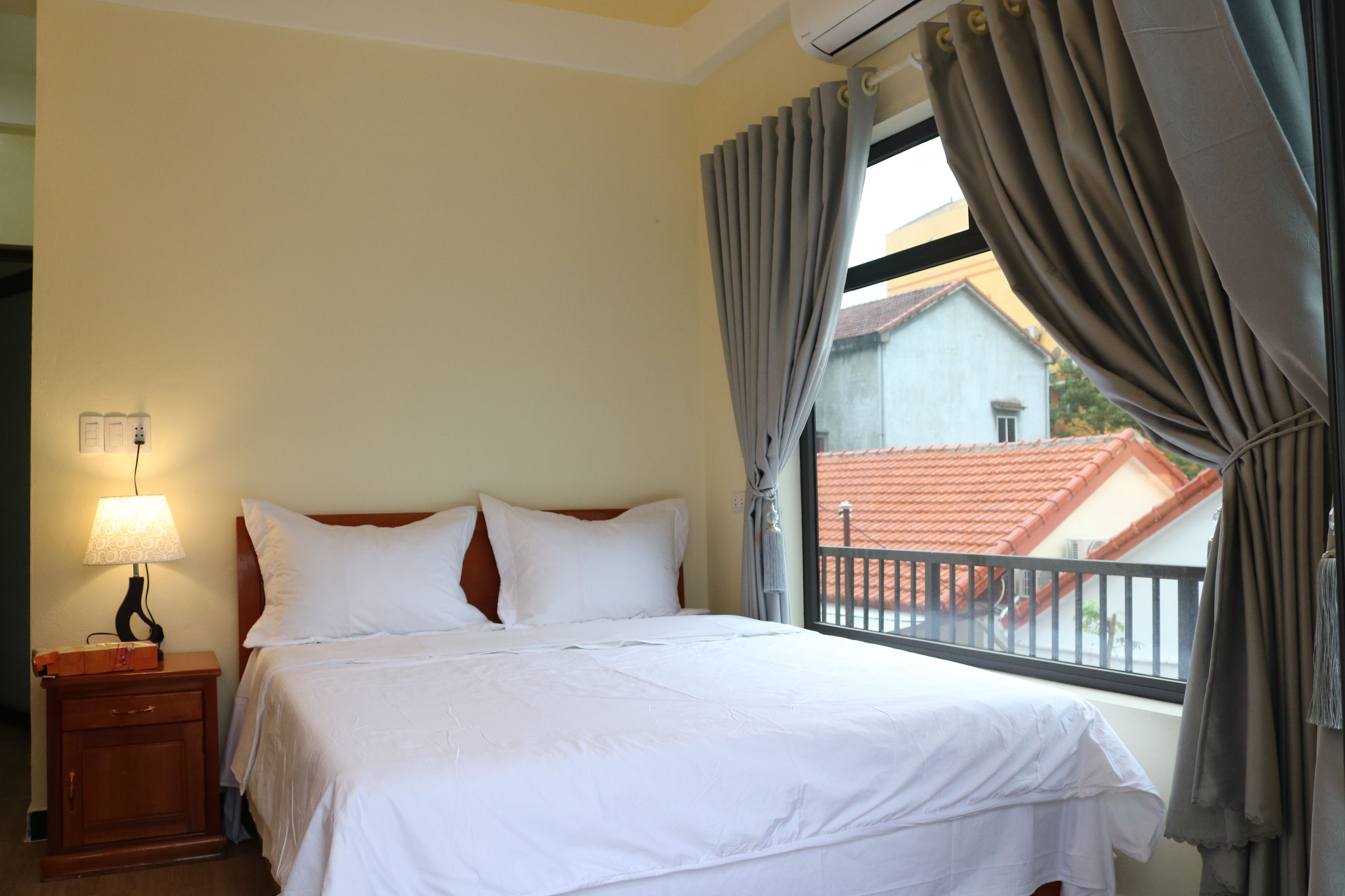 Una habitación de hotel con cama, mesita de noche con lámpara y ventana con cortinas.