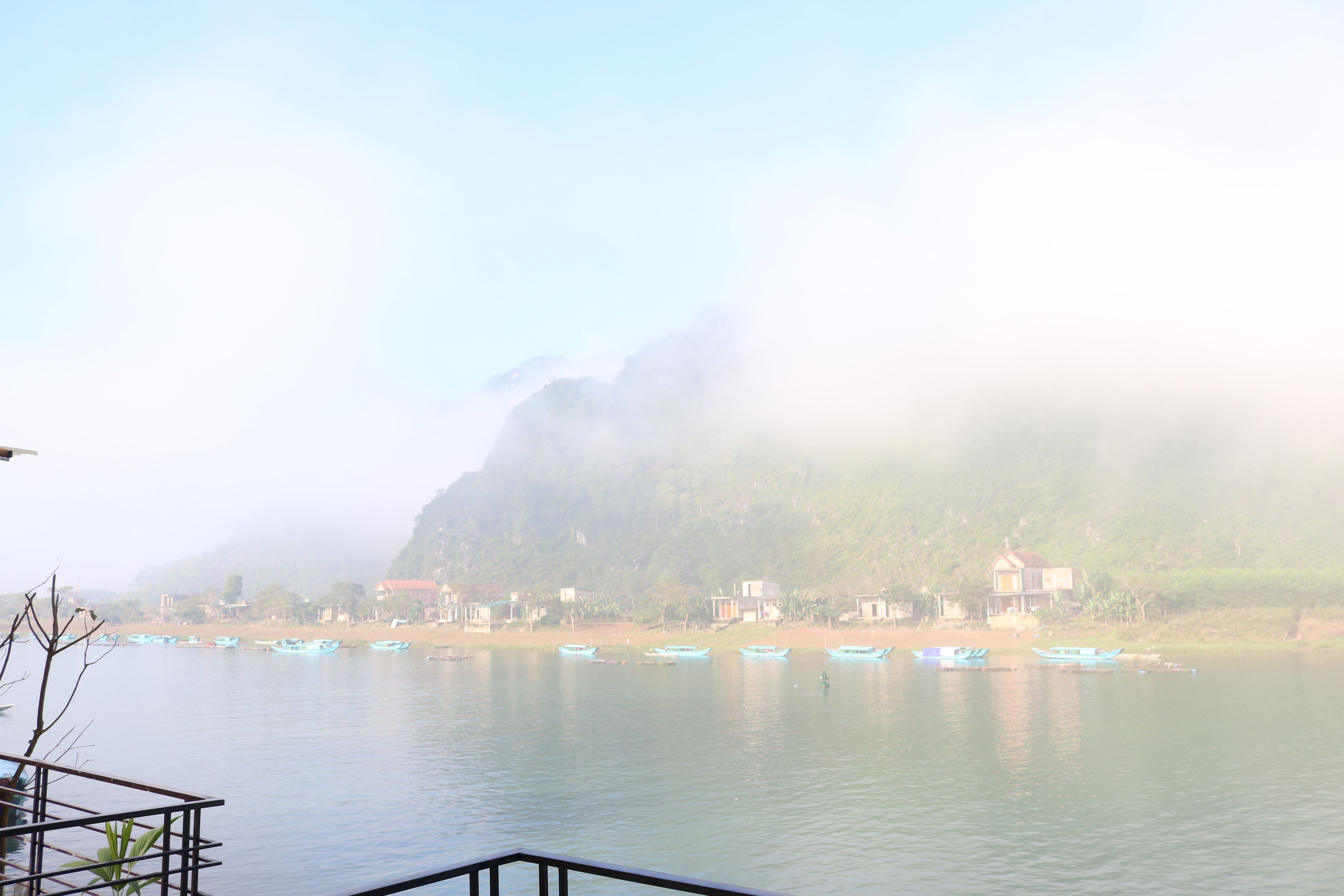 Un lago tranquilo con varias embarcaciones, un muelle de madera y edificios al fondo.