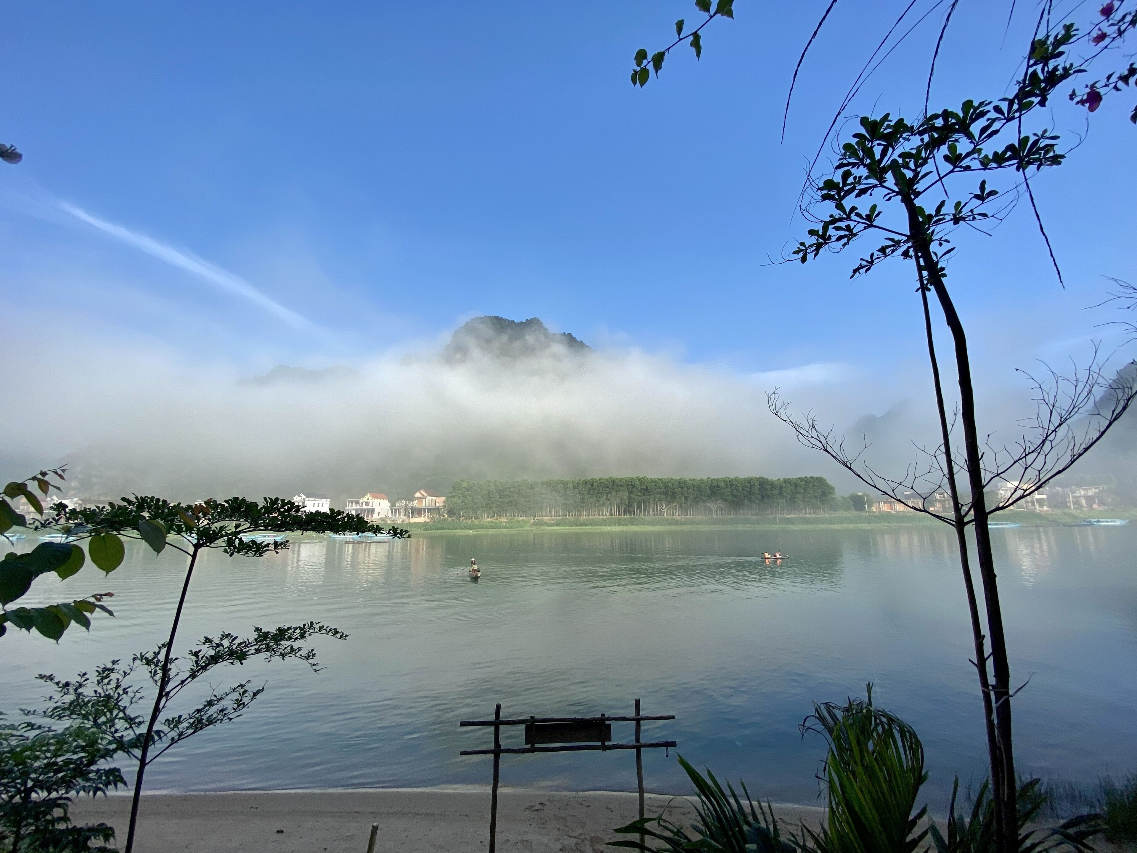 Ein friedlicher See mit Bank, ruhigem Wasser und einem Berg, der teilweise im Nebel verschwunden ist.