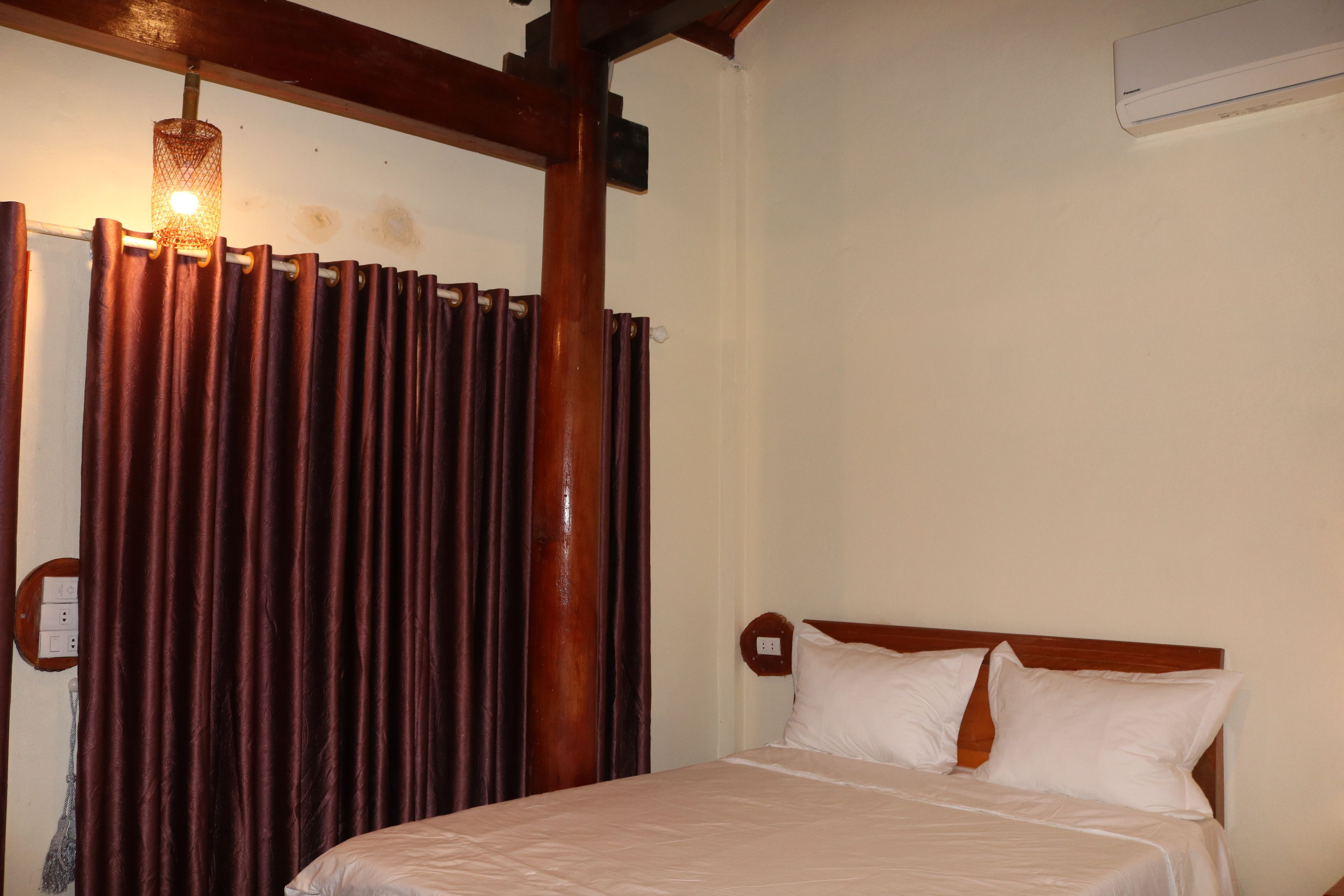 Habitación de hotel con estructura de cama de madera, cubrecama blanco y cortina con lámpara.