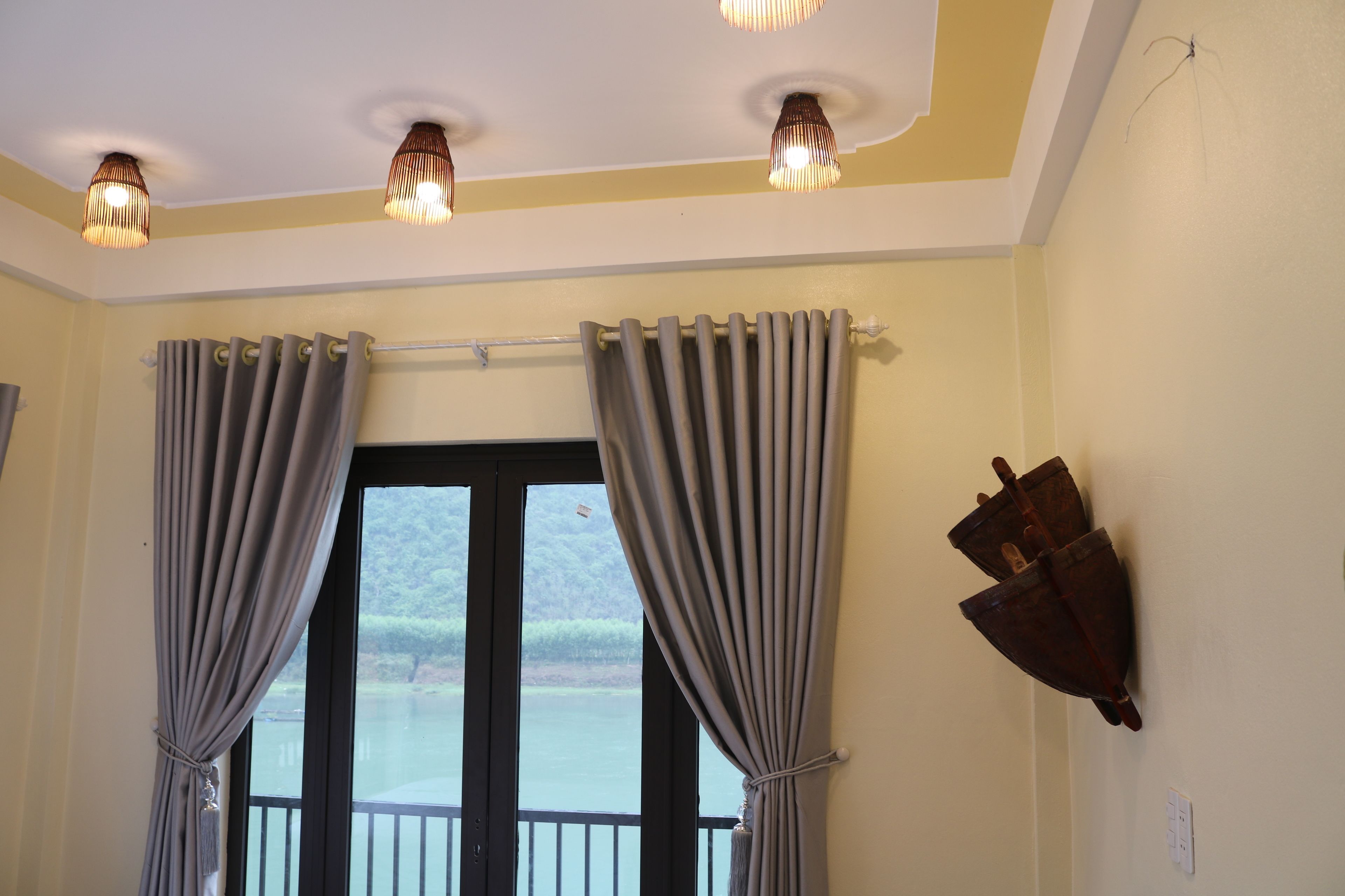 Une pièce dotée d’une grande fenêtre, de rideaux, d’un luminaire fixé au mur et d’un objet également fixé au mur.