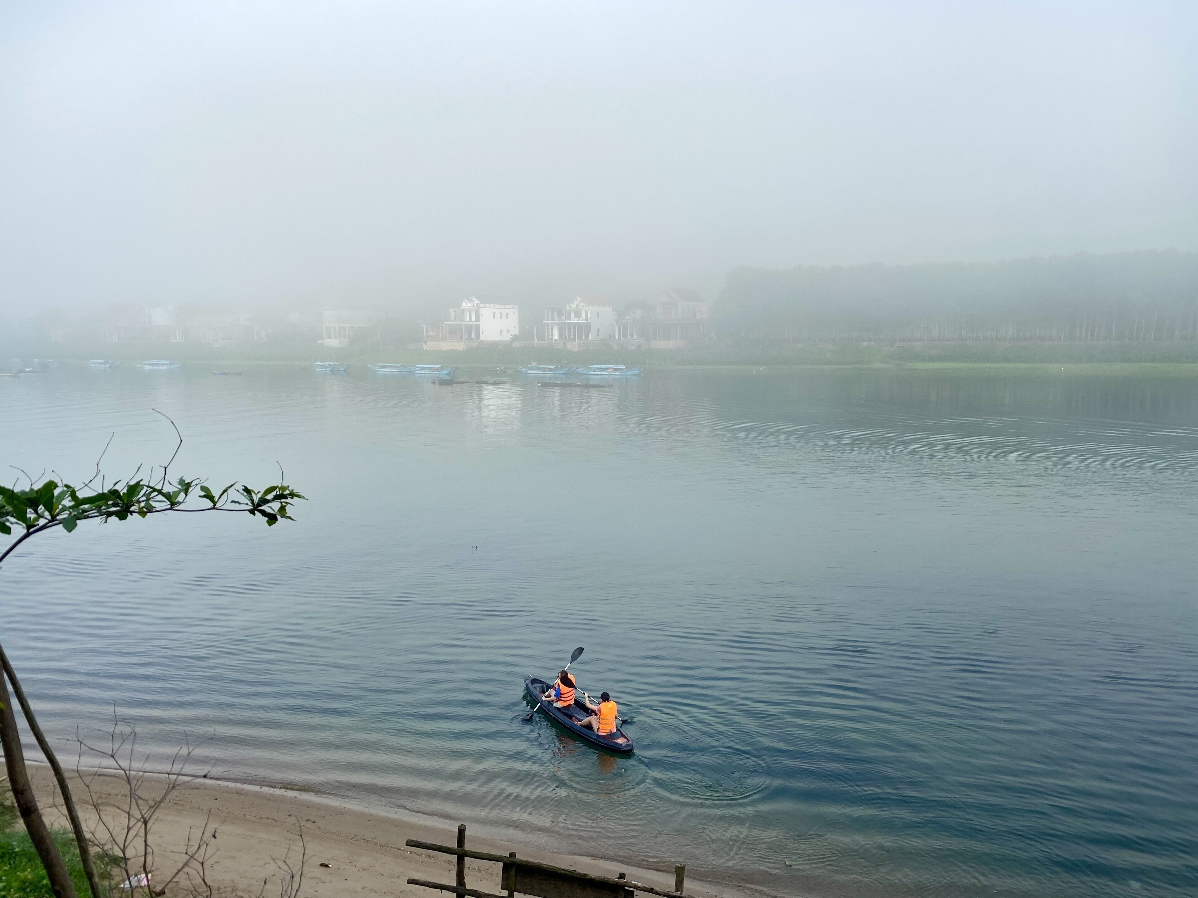 A calm lake with a single boat in the foreground and several buildings in the background.