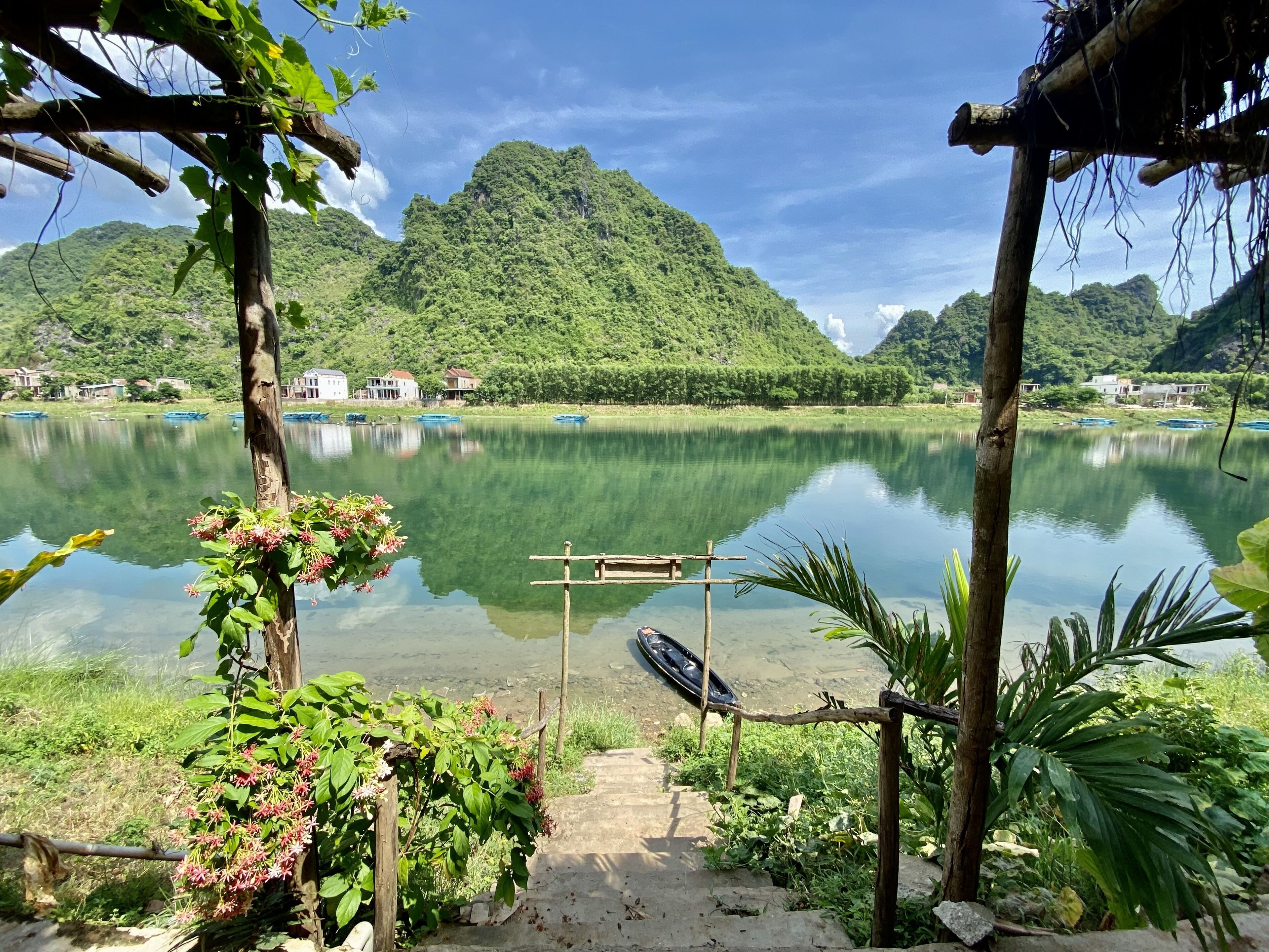 A tranquil lake with a wooden dock, surrounded by lush greenery and mountains.