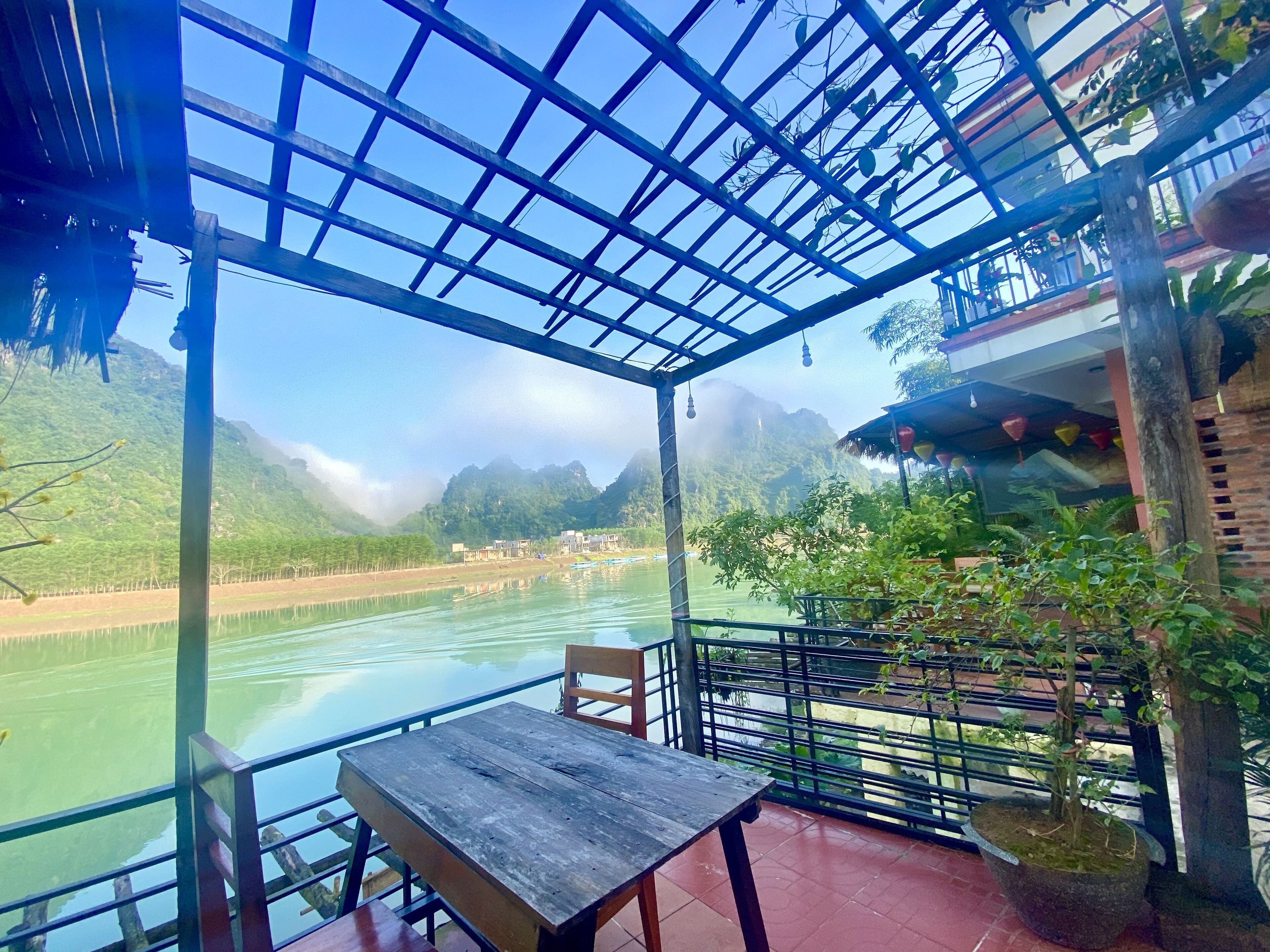 A covered outdoor area with a table and chairs, overlooking a river and mountains.