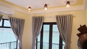 A room with a large window, grey curtains, and a view of a body of water. - Phong Nha Coco Riverside Homestay (Phong Nha)