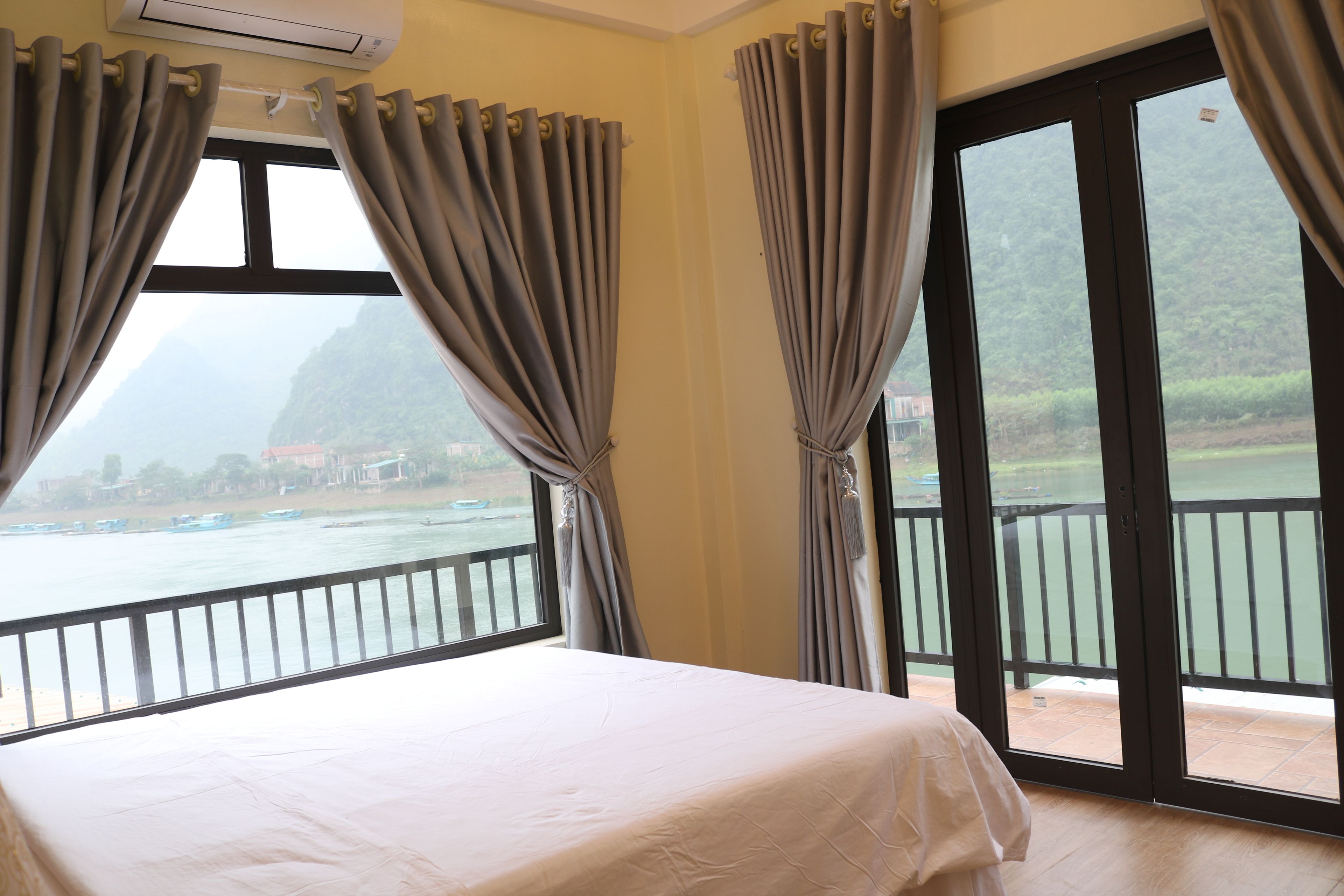 Une chambre avec un lit, de grandes fenêtres et une vue sur un plan d’eau et des montagnes.