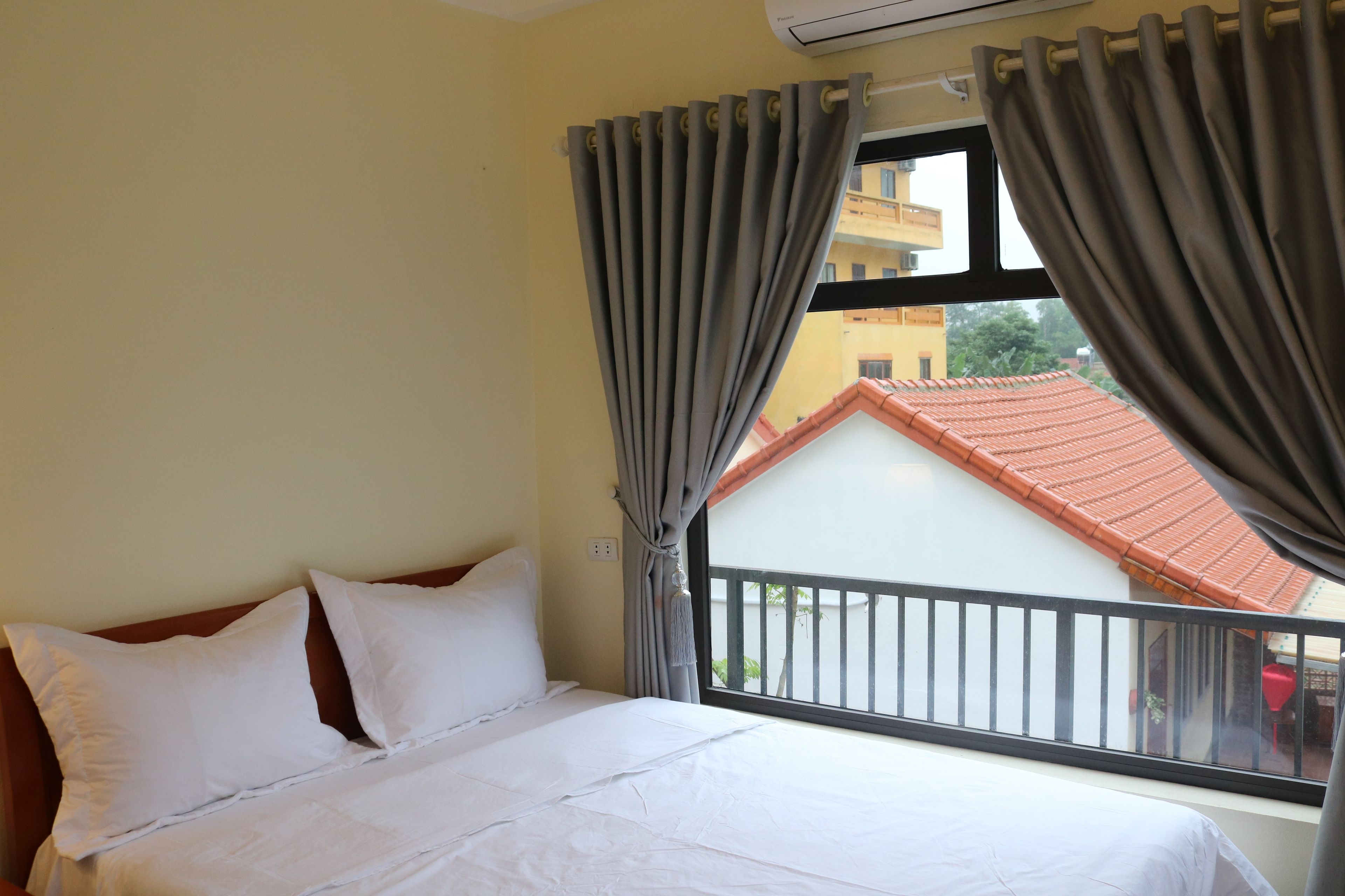 A hotel room with a bed, curtains, and a window with a view of a building and a balcony.