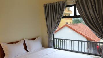 A hotel room with a bed, curtains, and a window with a view of a building and a balcony.
