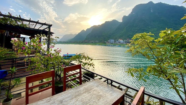 A terrace with a view of a calm lake, surrounded by mountains and a wooden pergola. - Phong Nha Coco Riverside Homestay (Phong Nha)