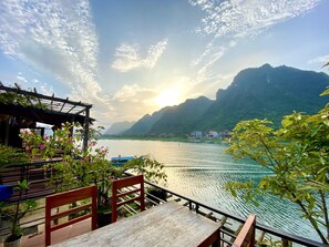 A terrace with a view of a calm lake, surrounded by mountains and a wooden pergola. - Phong Nha Coco Riverside Homestay (Bo Trach)