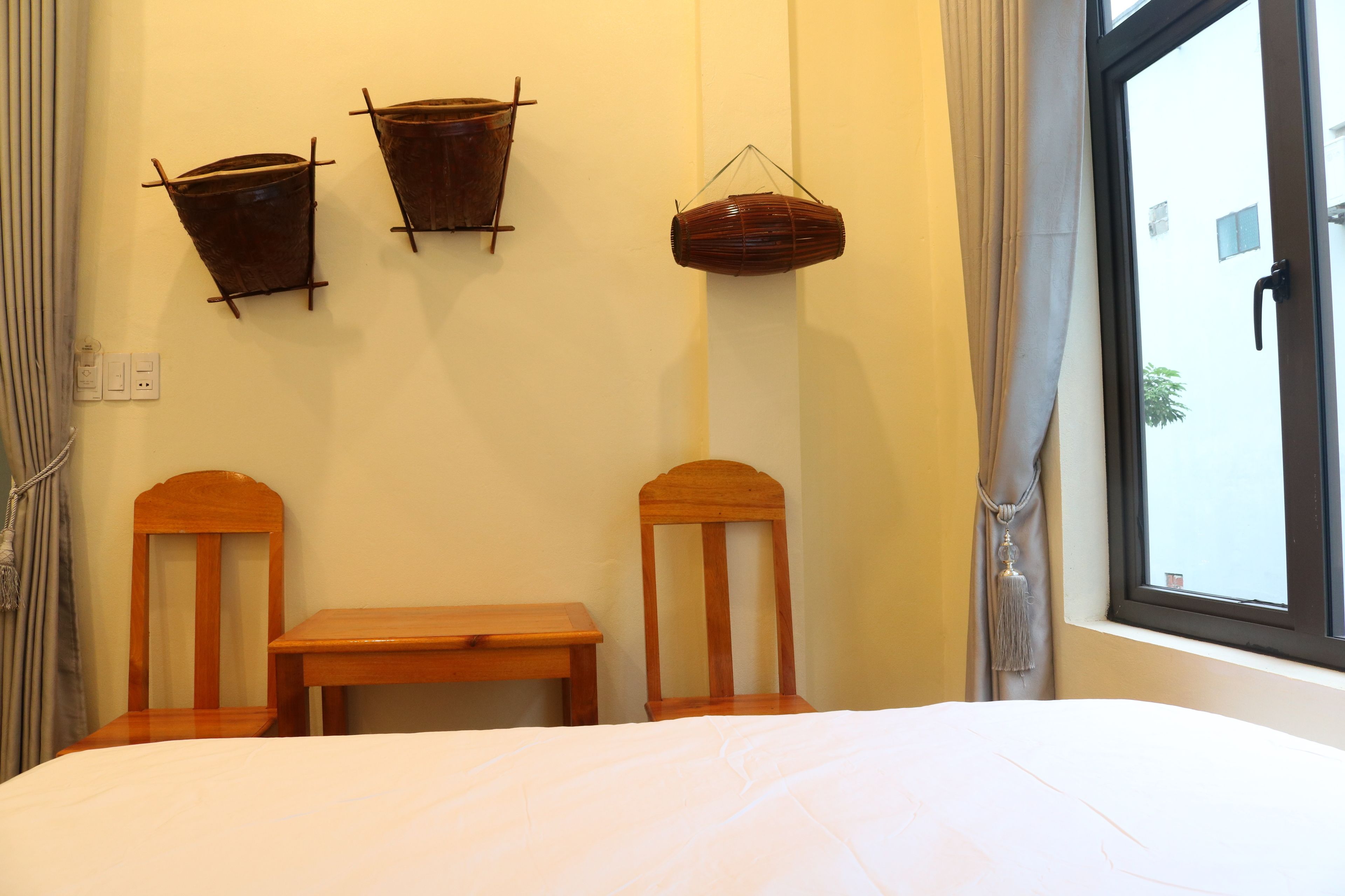 A room with a bed, two wooden chairs, a small table, and three wall-mounted baskets.