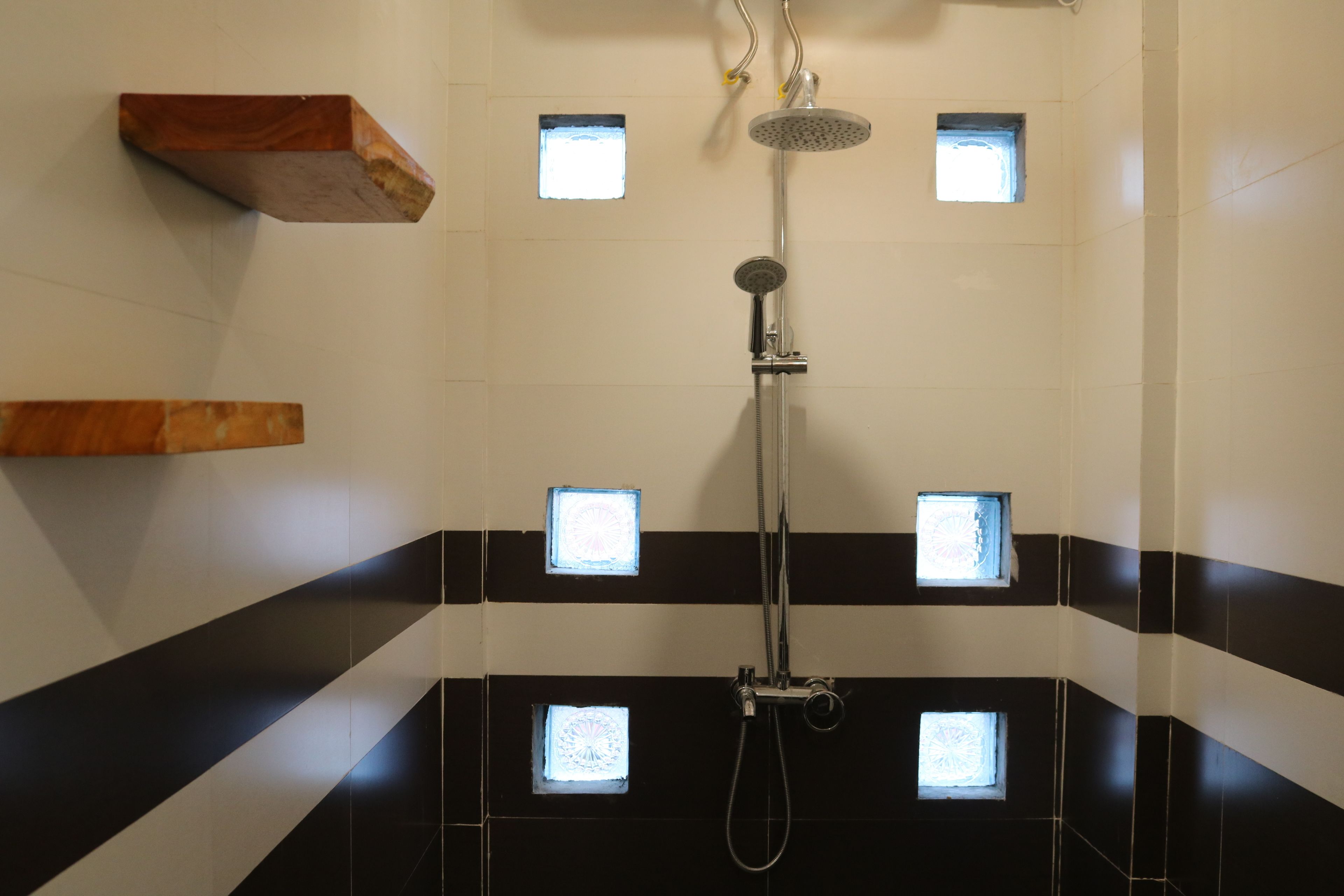 Un bagno con doccia, piastrelle a righe bianche e nere e piccole finestre quadrate.