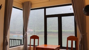 A room with a large window, two wooden chairs, and a table. - Phong Nha Coco Riverside Homestay (Phong Nha)