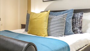 A neatly made bed with a blue bedspread and multiple pillows, including a yellow one. - Tudors eSuites Birmingham Apartments with Parking (Birmingham)