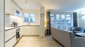 A modern kitchen with white cabinets, a built-in oven, and a window with blinds. - The Faculty Apartments (Reading)