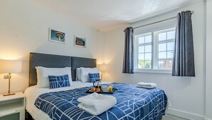 A neatly made bed with a blue and white geometric bedspread, a tray with croissants and orange juice, and a white towel on the bed. - The Faculty Apartments (Reading)