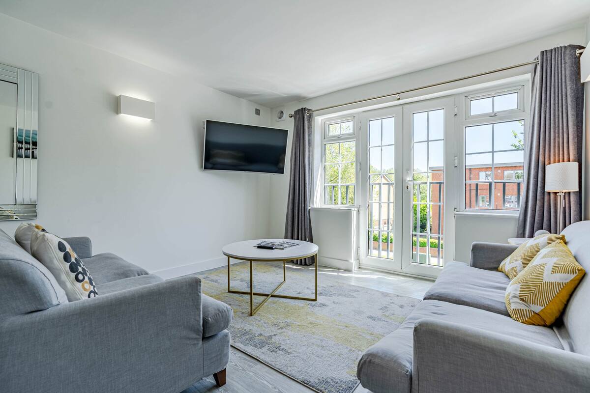 A modern living room with a grey sofa, a round coffee table, and a flat-screen TV mounted on the wall.