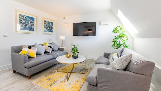 A modern living room with a grey sofa, a round coffee table, and a flat-screen TV mounted on the wall. - The Faculty Apartments (Reading)