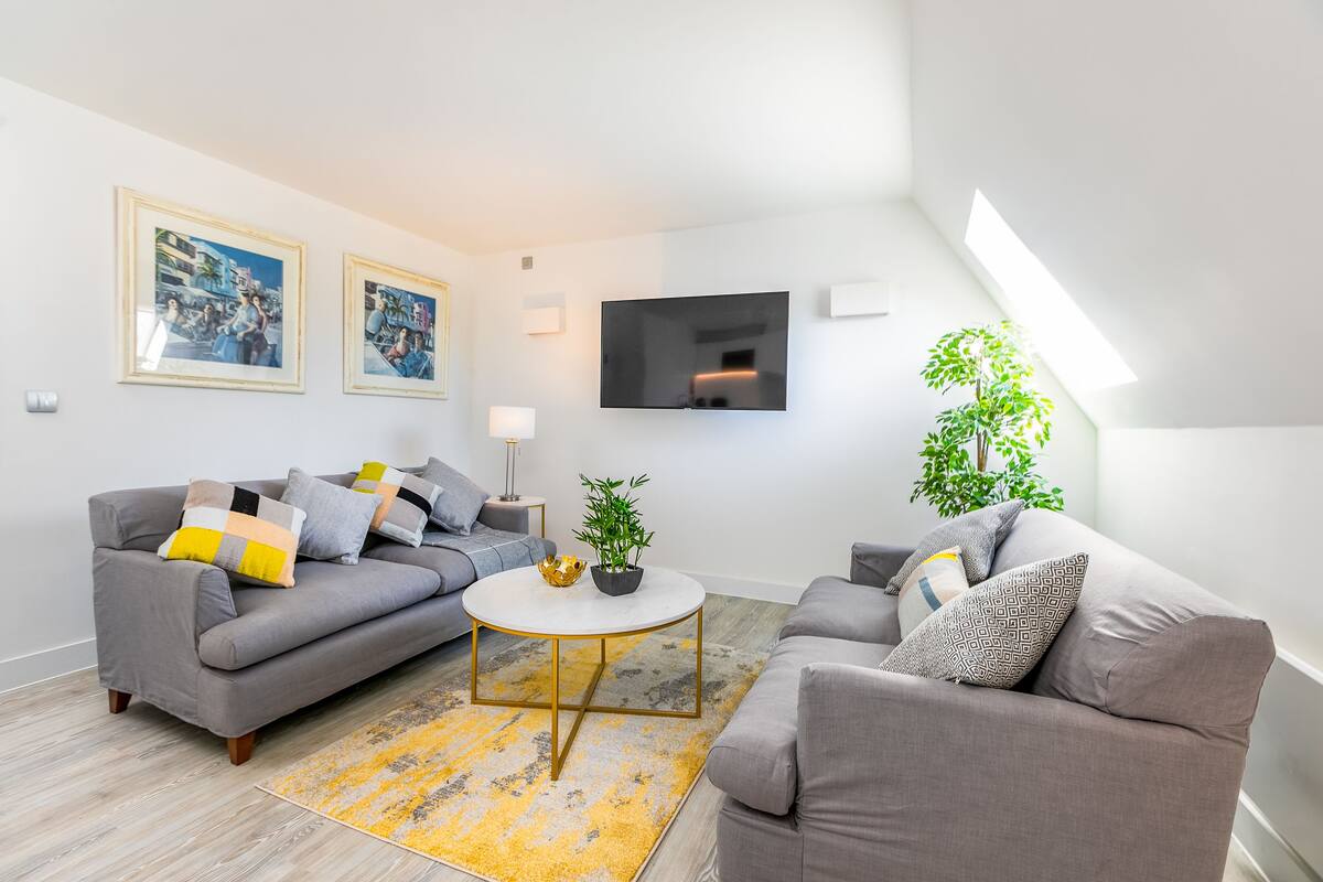 A modern living room with a grey sofa, a round coffee table, and a flat-screen TV mounted on the wall.