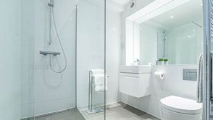 A modern bathroom with a glass shower enclosure, a white toilet, and a vanity with a mirror. - The Faculty Apartments (Reading)