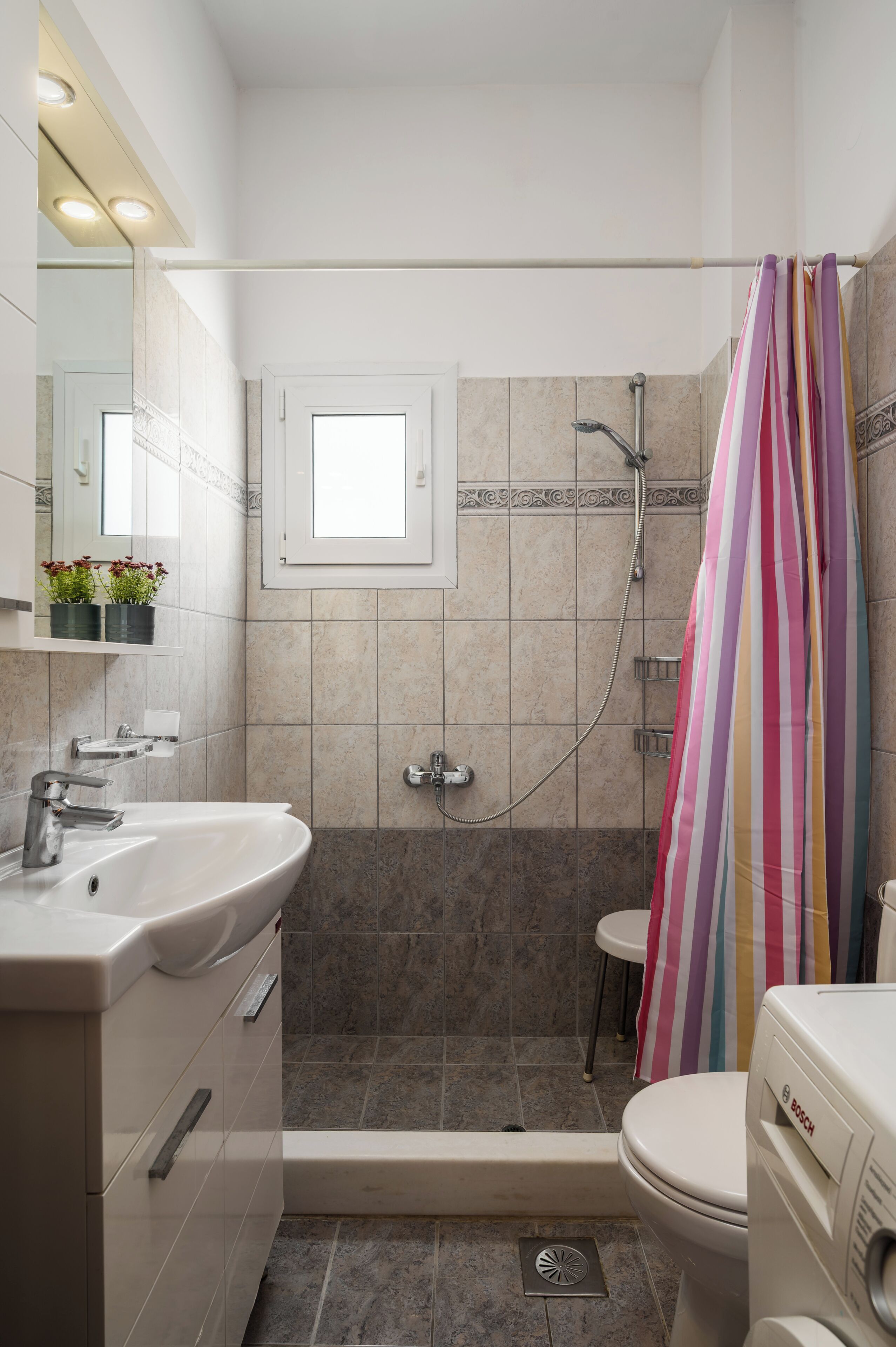 Un bagno con doccia, WC, lavandino e finestra.