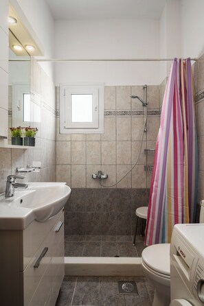 Ein Badezimmer mit Dusche, Toilette, Waschbecken und einem Fenster.