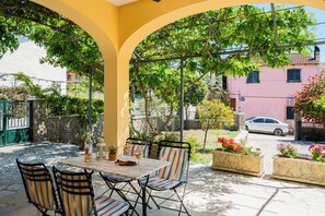 Eine Außenpatio mit Tisch und Stühlen, umgeben von Grünpflanzen und einem rosafarbenen Gebäude im Hintergrund.