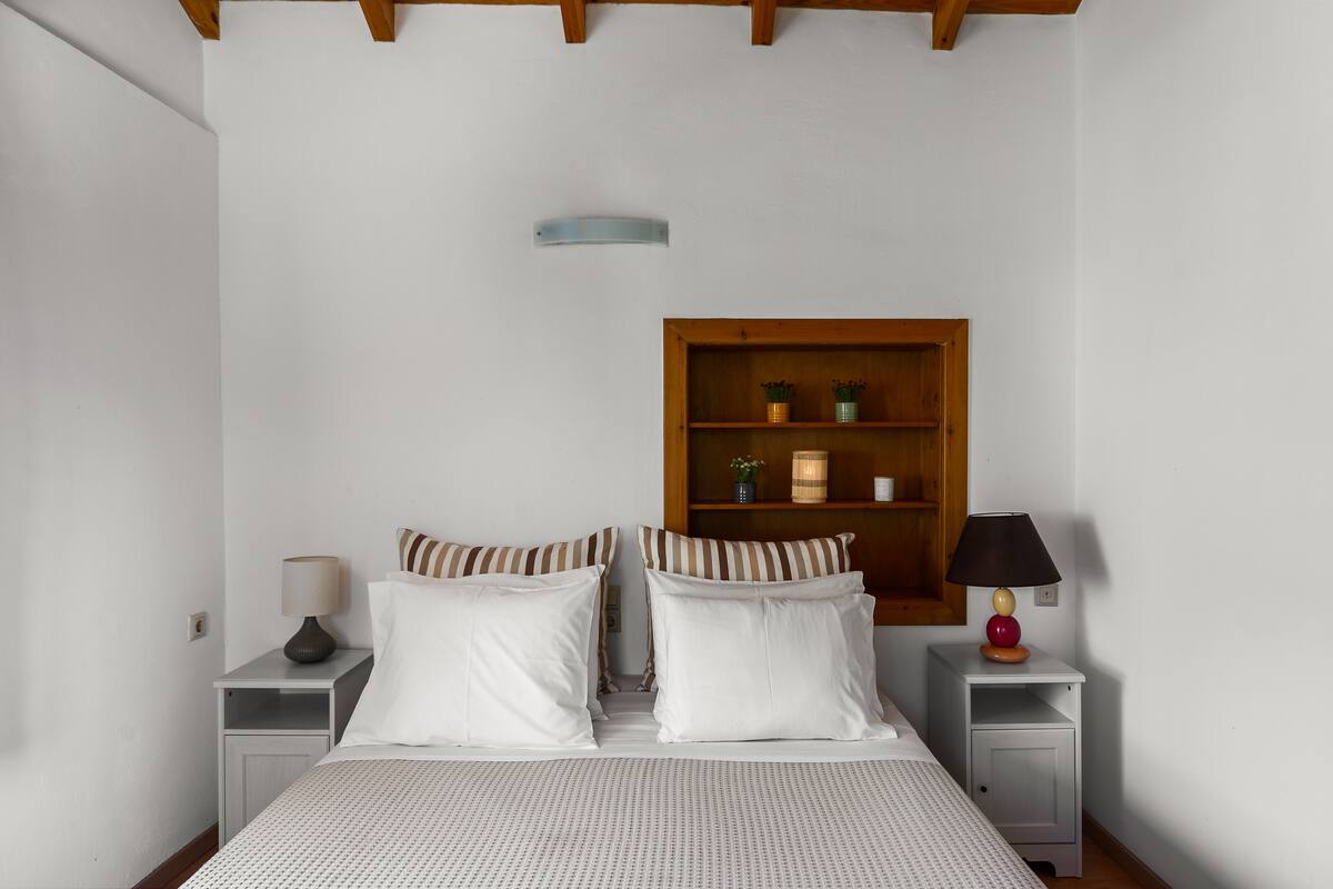 Ein Schlafzimmer mit einem Bett, zwei Nachttischen, einem kleinen Tisch, einer Holzablage und einer Lampe.