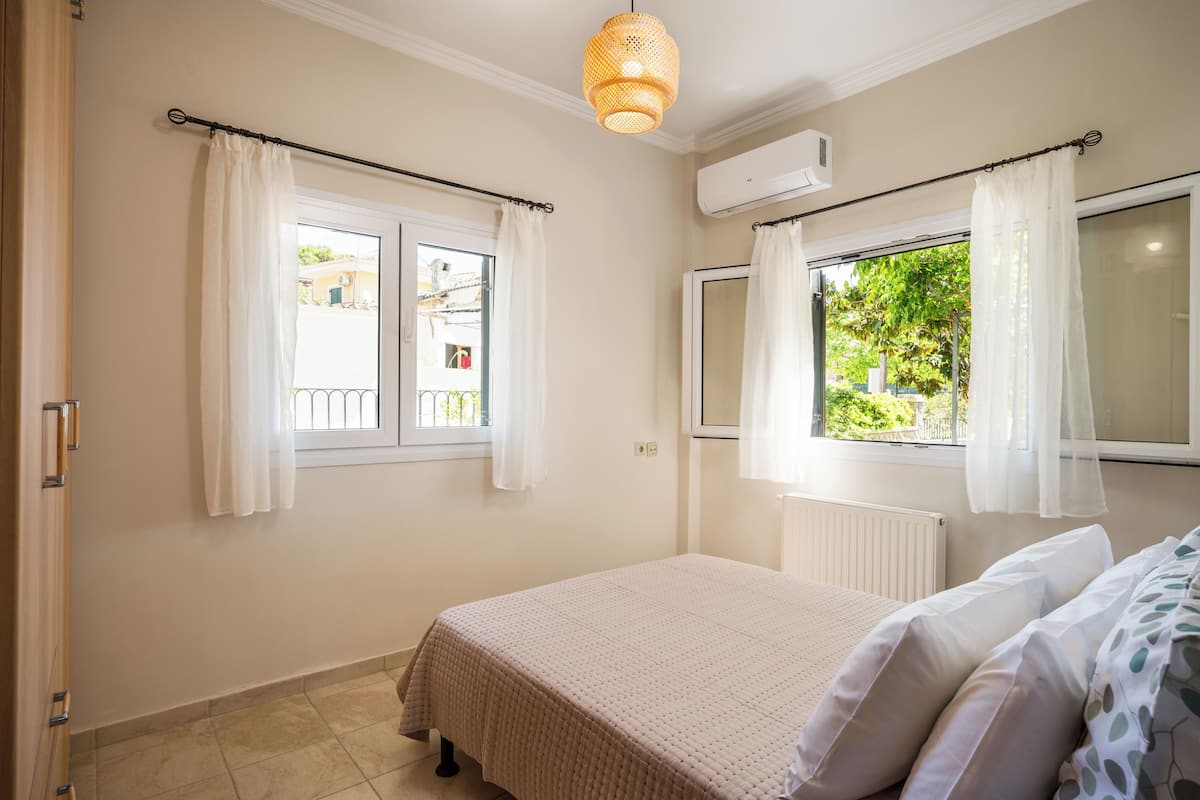 Ein Schlafzimmer mit einem Bett, zwei Fenstern mit Vorhängen, einer Klimaanlage und einem Heizkörper.