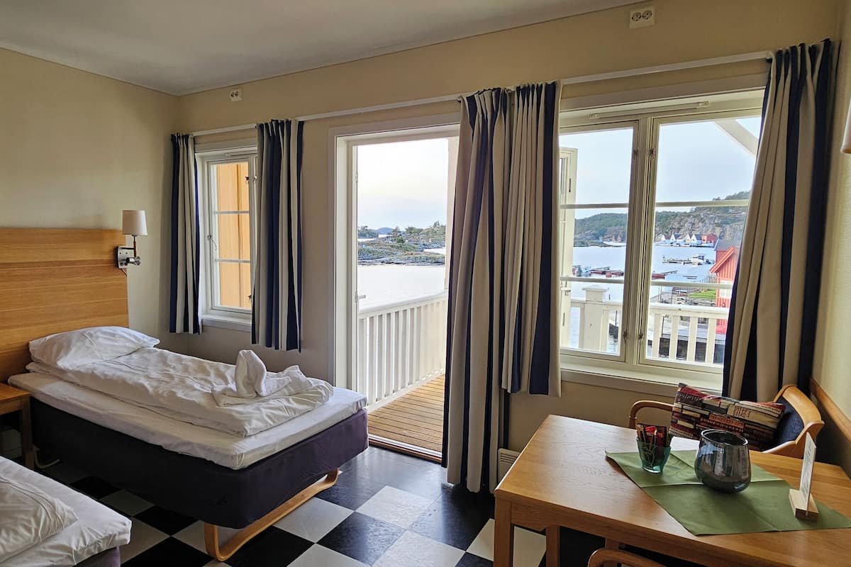 Une chambre d’hôtel avec un lit, une tête de lit en bois, une table avec une lampe et une vue sur un port.