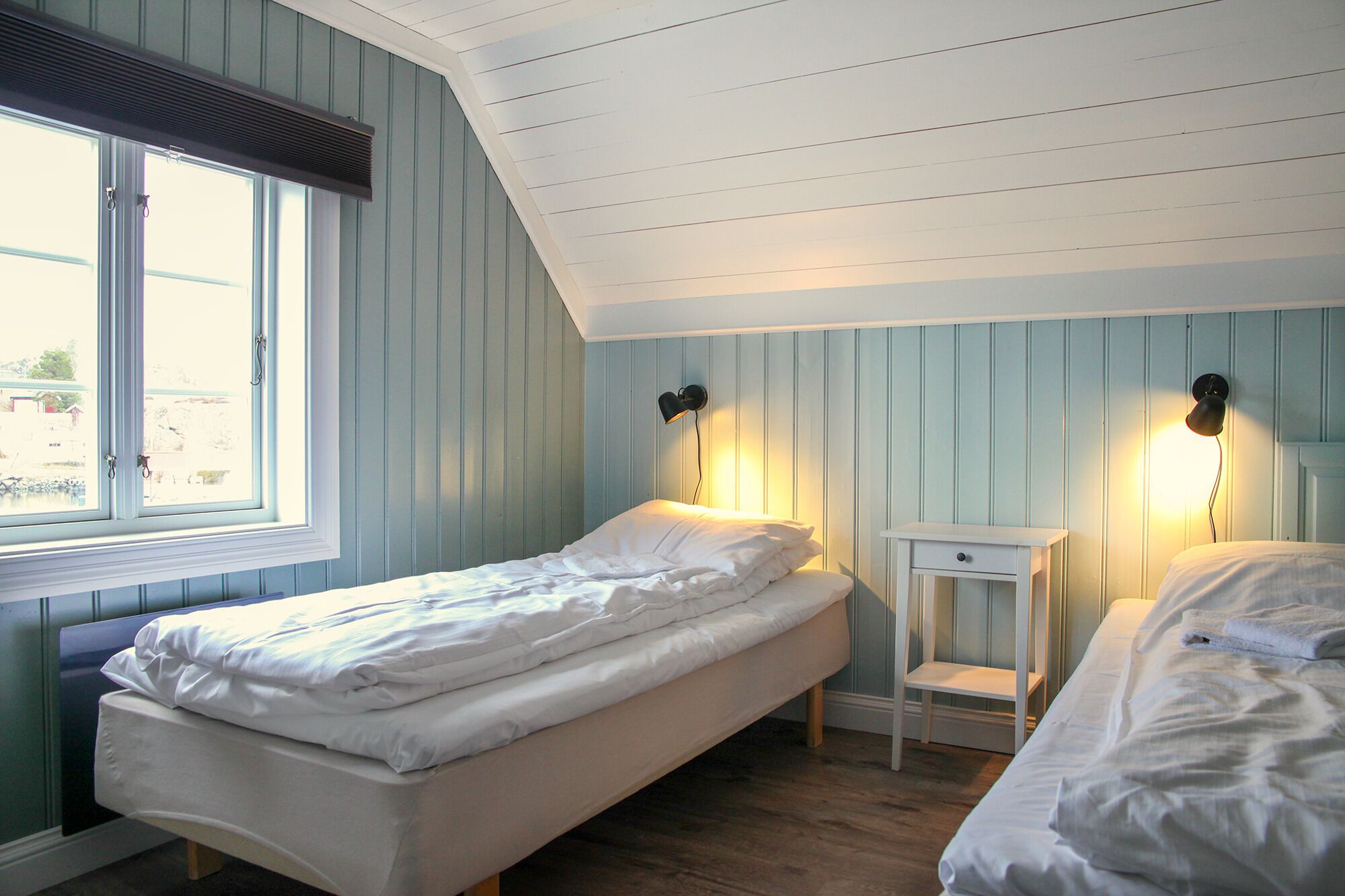 Une chambre avec deux lits, une fenêtre et une petite table de chevet avec une lampe.